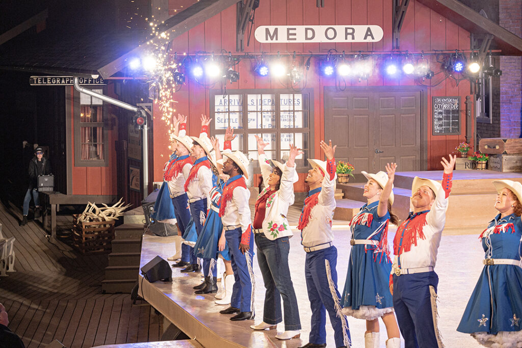 Performers dressed in patriotic red, white, and blue costumes stand in a line with arms outstretched as sparks fly at the Medora Musical, a popular entertainment attraction in Medora, North Dakota
